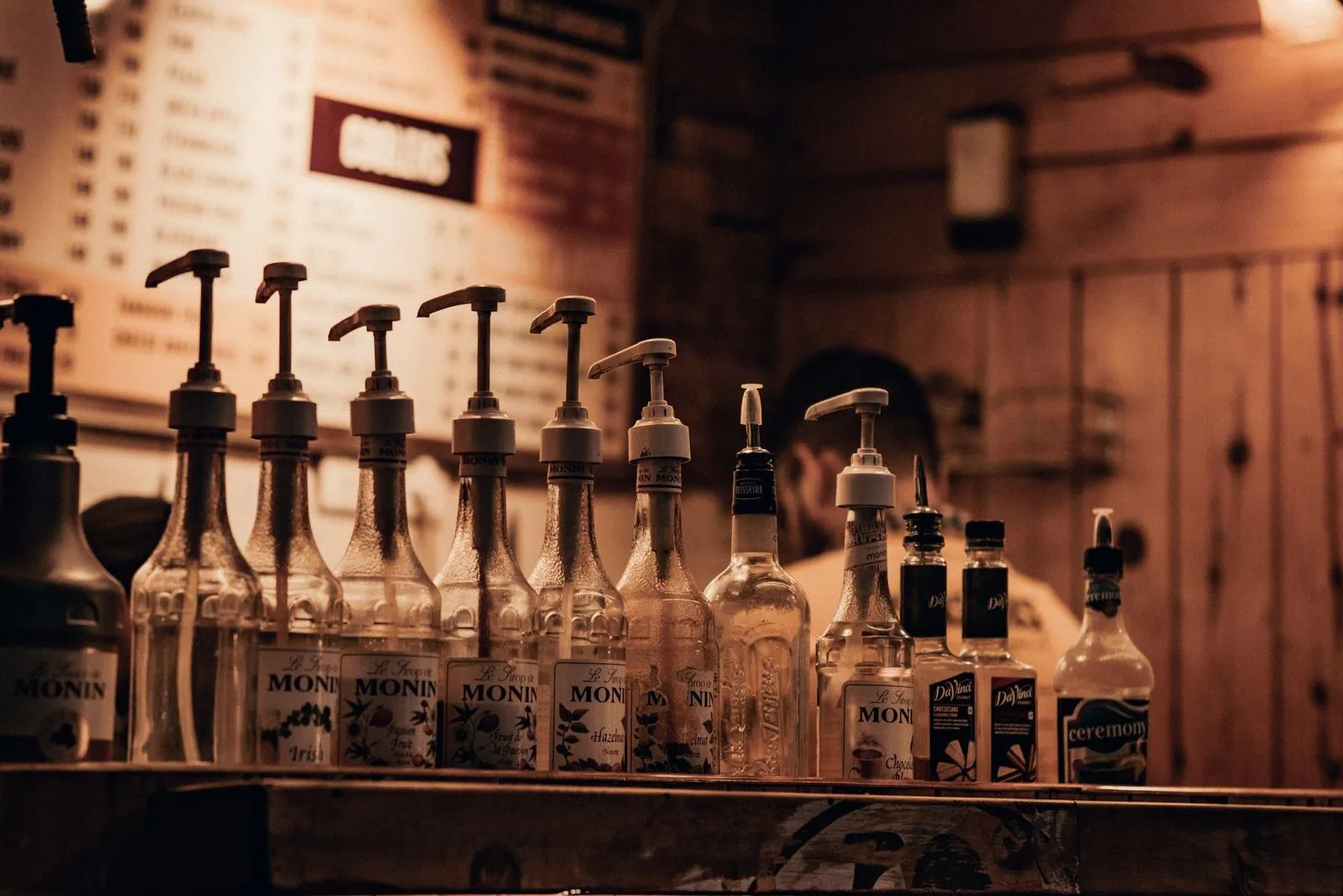 A rustic bar counter with syrup bottles and hanging lamps, a wall TV showing The Copper Tap tap list